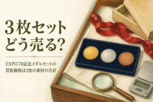 ケースに並んだ無地の金色・銀色・銅色のメダル3枚のイメージ、「3枚セットどう売る？」の文字